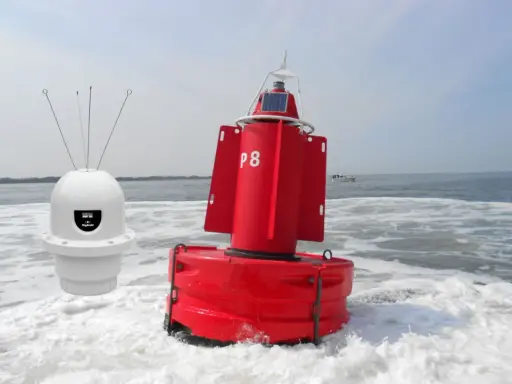 Deux bouées, une blanche avec des antennes et une rouge marquée "P8", flottent sur l'eau agitée, un petit bateau à l'horizon.