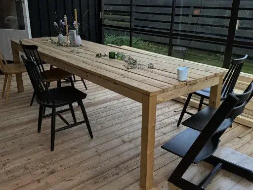 Ett träbord och stolar på en altan. Bordet är dekorerat med blommor och ljus. Perfekt för att behandla furu utomhus och njuta av sommaren.