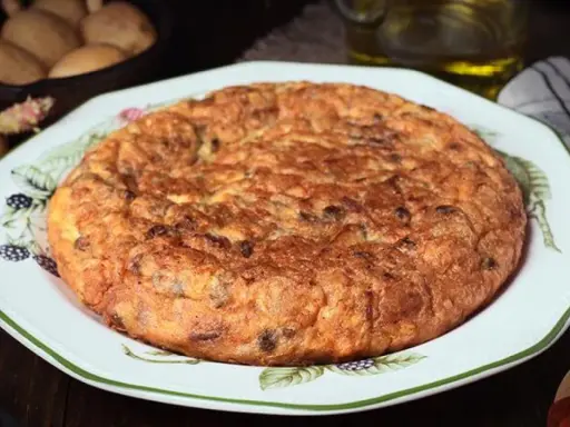 Tortilla española, un clásico de la comida típica de Granada, servida en un plato decorado. Patatas y aceite en el fondo.