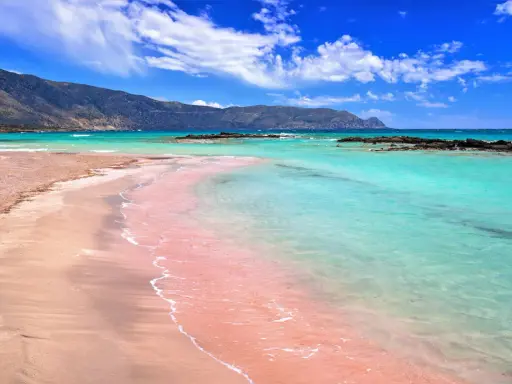 Różowa plaża Kreta kusi turkusową wodą i piaszczystym brzegiem. Góry w tle dodają uroku.