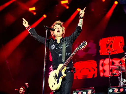 Billie Joe Armstrong, en av medlemmar av Green Day, sjunger och spelar gitarr på scenen under en konsert, upplyst av röda strålkastare.
