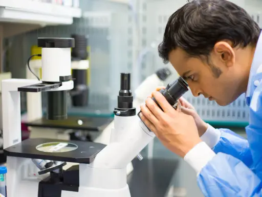 Mężczyzna w niebieskim fartuchu laboratoryjnym patrzy przez mikroskop.