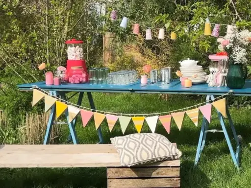 Une table bleue dressée pour une deco garden party à faire soi même, avec guirlandes, bonbons et fleurs.