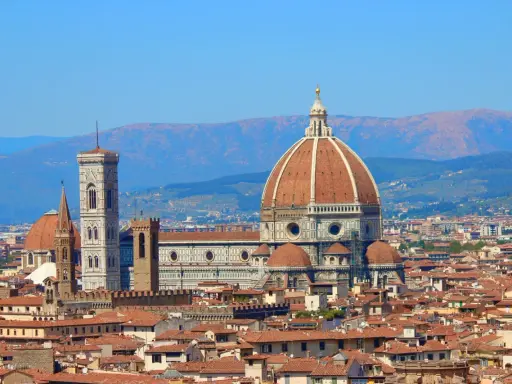 Vue panoramique de Florence avec le **dôme de Brunelleschi** dominant la ville, sous un ciel bleu clair.