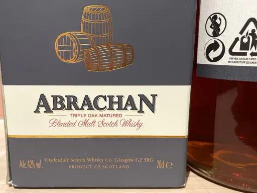 Elegancka butelka Abrachan Blended Malt Scotch Whisky, potrójnie dojrzewająca w dębie, z beczkami na etykiecie.