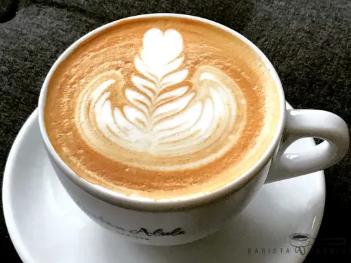Eine Tasse Cappuccino mit kunstvoller Barista Art, die ein Herz und Blätter zeigt.