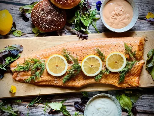 Flammlachs mit Zitronenscheiben und Dill, serviert mit cremigen Dips und frischem Salat als Beilagen.