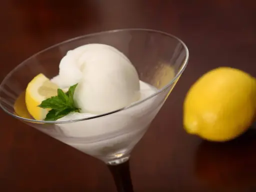 Glace colonel rafraîchissante dans un verre à martini, garnie d'une tranche de citron et de menthe. Un citron entier est posé à côté.
