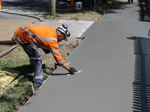 Robotnik wygładza świeży beton, zastanawiając się, ile kosztuje kubik betonu na nową ścieżkę.