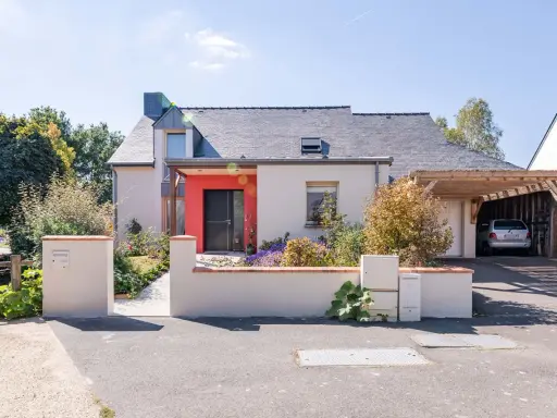 Maison moderne avec entrée rouge vif et carport en bois. Idéal pour estimer le prix rénovation maison m2.