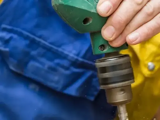 Dłoń trzyma wiertarkę, pokazując, jak włożyć wiertło do wiertarki.