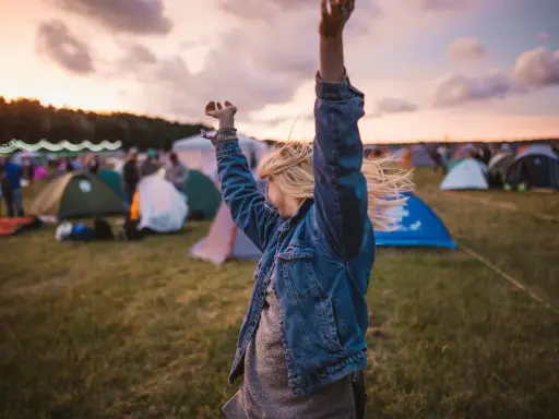 Ragazza con le braccia alzate in un campo di tende, immersa nell'atmosfera di uno dei festival techno più famosi.