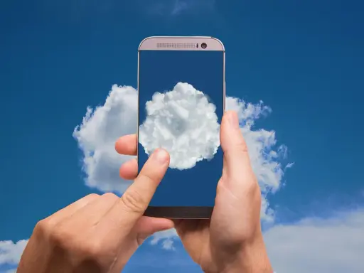 Dłonie trzymają telefon, na którego ekranie widać chmurę. To symbol tego, gdzie jest chmura w telefonie - w chmurze danych.
