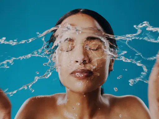 Una mujer se lava la cara con agua fría, sintiendo el frescor en su piel.