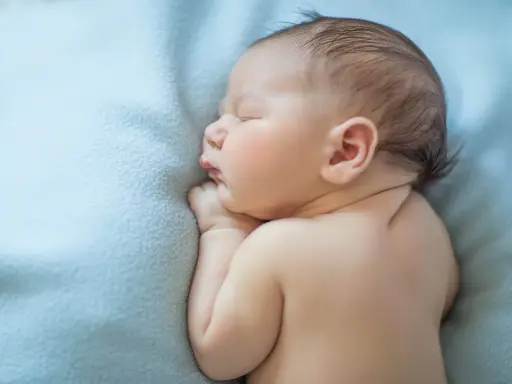 Śpiący skrajny wcześniak na błękitnym kocyku. Delikatne rysy twarzy, małe rączki złożone pod brodą.