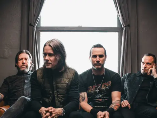 Alter Bridge Sverige: bandmedlemmar sitter på en soffa framför ett fönster.