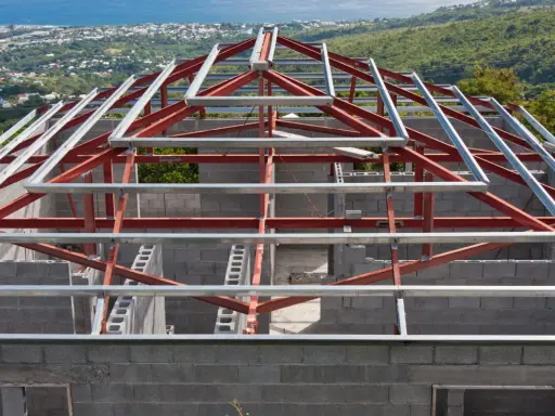 Structure métallique d'une maison en construction, avec des poutres rouges et grises. Un inconvénient potentiel de ce type de maison est la nécessité d'une isolation thermique soignée.