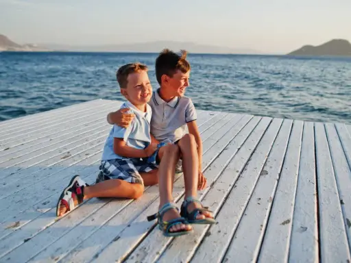 Dos niños sonríen sentados en un muelle blanco. ¡Ideas para que hacer en Murcia con niños!