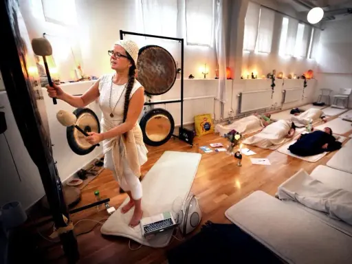 En kvinna spelar gong för en grupp liggande deltagare. Ljudvågorna sprider sig som **ra ma da sa** och skapar en lugn atmosfär.