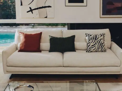 Sofá blanco con cojines decorativos: uno rojo, uno verde con textura y otro con estampado de cebra.