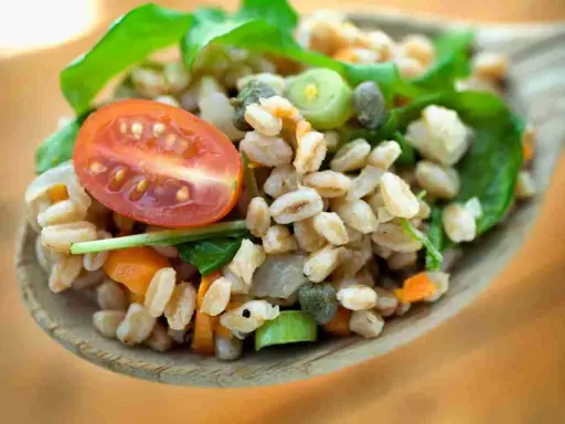 Un cucchiaio di farro condito con pomodorini, capperi e verdure fresche. Un'idea gustosa su come condire il farro per un pasto leggero e nutriente.