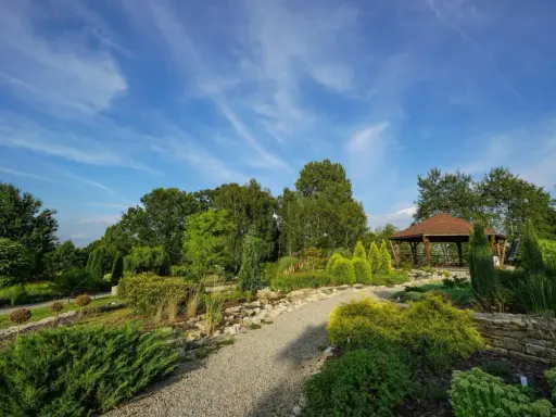 Malownicze ogrody botaniczne na Śląsku z altaną i kamiennymi ścieżkami, otoczone bujną zielenią pod błękitnym niebem.