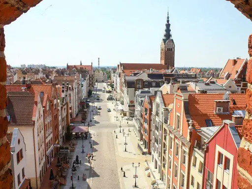 Widok z góry na urokliwą elbląg starówkę z kolorowymi kamieniczkami i wieżą kościelną w tle.