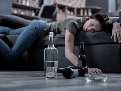 Kobieta leży nieprzytomna na kanapie, obok butelki i szklanka. Czy alkoholik może pić kontrolowanie? To pytanie pozostaje bez odpowiedzi.