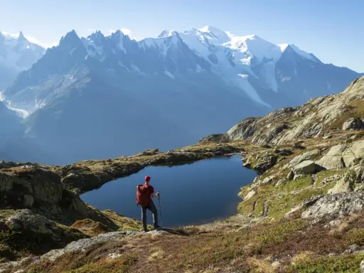 Widok na wejście na Mont Blanc. Turysta z plecakiem i kijkami stoi nad górskim jeziorem, podziwiając ośnieżone szczyty.
