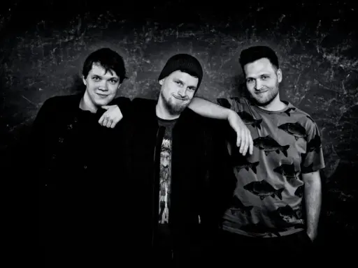 Trzech młodych mężczyzn pozuje do zdjęcia w **acid wizard studio**. Jeden z nich ma na sobie czarną kurtkę, drugi czapkę i koszulkę z nadrukiem, a trzeci koszulkę w ryby.