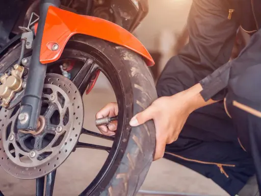Sprawdzanie, jakie ciśnienie w oponach motocyklowych jest kluczowe dla bezpieczeństwa. Dłoń z manometrem przy wentylu przedniego koła.
