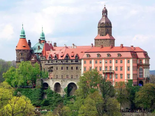 Malownicze zamki i pałace wokół Wrocławia, jak ten imponujący kompleks z wieżami i czerwonymi dachami, zachwycają architekturą i otoczeniem.