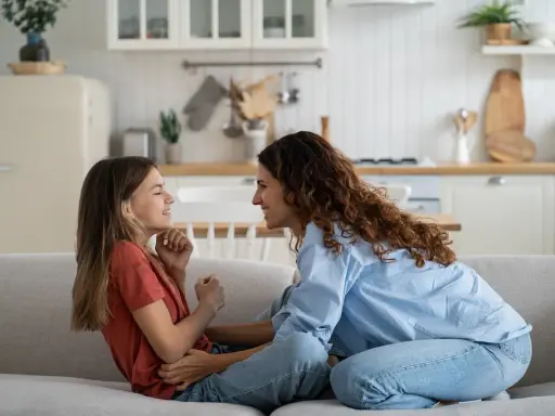 Madre e hija ríen en el sofá. Ella le enseña como es la primera regla de una niña: la empatía.