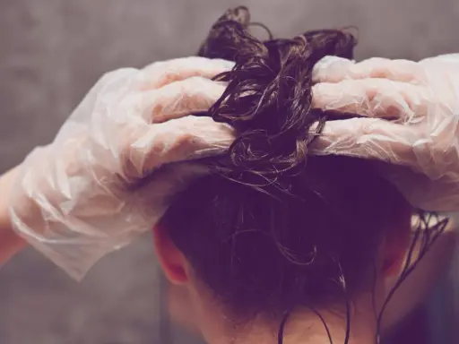 Hände mit Handschuhen tragen Olaplex Nr. 3 auf nasses, dunkles Haar auf.