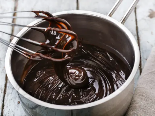 Fouet mélangeant du chocolat noir brillant dans une casserole, étape clé pour le tempérage.