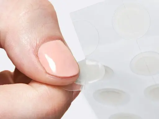 Une main retire délicatement un patch boutons d'une feuille, prêt à agir contre les imperfections.
