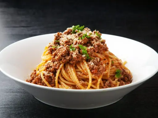 Pyszny makaron z mięsem mielonym, posypany parmezanem i natką pietruszki, podany w białej misce.
