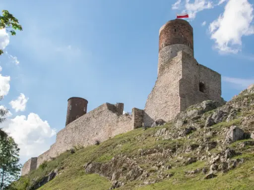 Ruiny zamku na skalistym wzgórzu w paśmie gór świętokrzyskich. Biało-czerwona flaga powiewa na wieży.