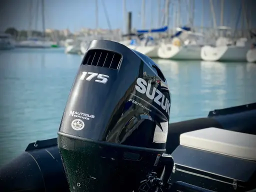 Moteur hors-bord Suzuki 175 CV, prêt pour une longue journée sur l'eau. Le mât de l'arbre est visible, avec des voiliers en arrière-plan.