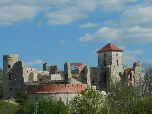 Zamek Tenczyn, ruiny kamiennej twierdzy z czerwoną cegłą i polską flagą, na tle błękitnego nieba z chmurami.