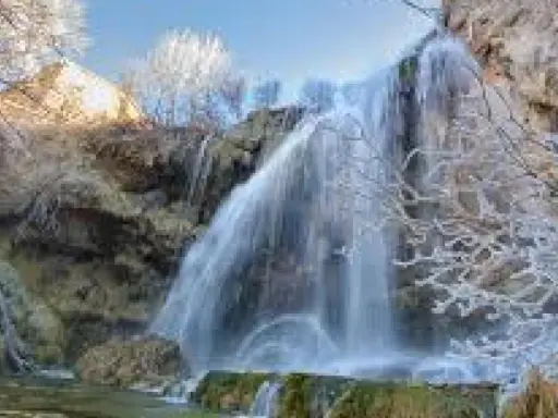 Cascada helada en el nacimiento del río Júcar, con ramas cubiertas de escarcha y agua cayendo sobre rocas.