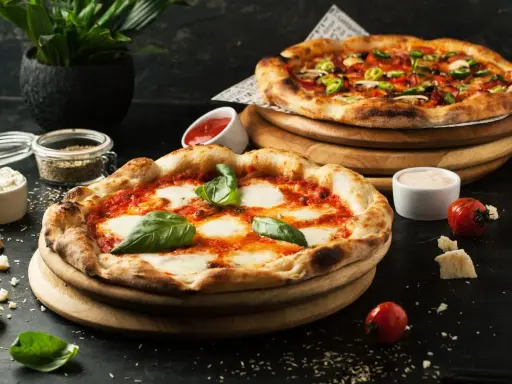 Dwie pyszne pizze, jedna margherita, druga z dodatkami. Obok sosy i pomidorki, idealne dodatki do pizzy.