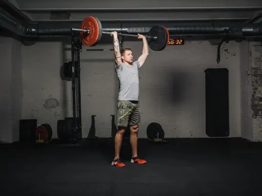 Mann führt einen **strict press** mit einer Langhantel im Fitnessstudio aus.