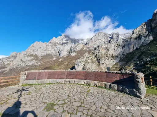 Impresionante mirador de los Picos de Europa con un muro de piedra y metal decorado. El sol ilumina las majestuosas montañas.
