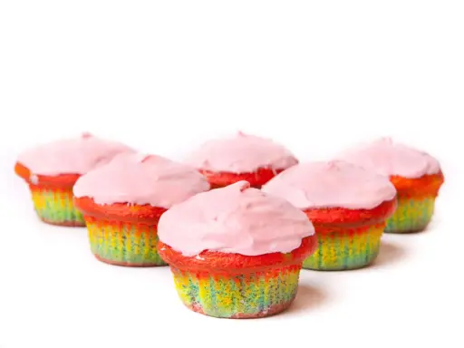 Bunte Muffins mit Lebensmittelfarbe und rosa Zuckerguss, die wie ein Regenbogen aussehen.