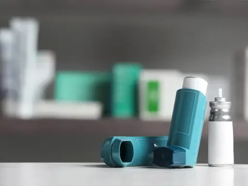 Zwei Inhalatoren, einer davon mit einem silbernen Behälter, liegen auf einer weißen Oberfläche. Sie sind wichtige Hilfsmittel bei der Behandlung von COPD, wo Cortison oft eine Rolle spielt.