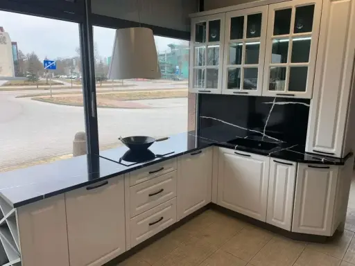 Elegancka biała kuchnia z czarnym blatem i efektownym czarnym panelem z białymi żyłkami. Wok na płycie indukcyjnej czeka na kulinarną przygodę.