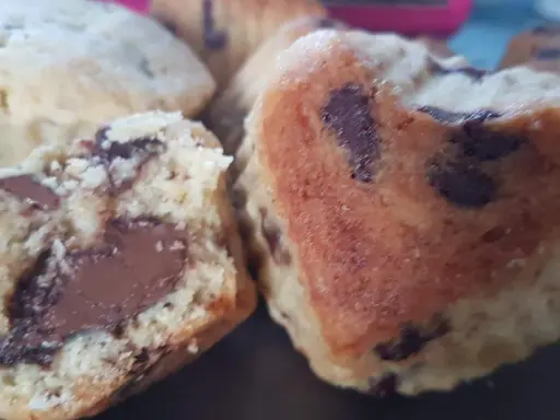 Gros plan sur des cookies moelleux en forme de cœur, débordant de pépites de chocolat. Un cookie est coupé en deux, révélant un cœur fondant.