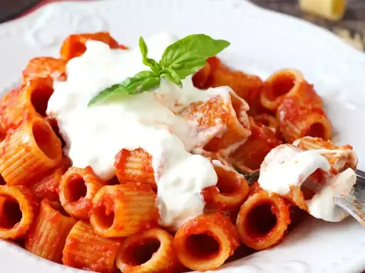 Rigatoni al sugo rosso con abbondante stracciatella cremosa e una fogliolina di basilico fresco.