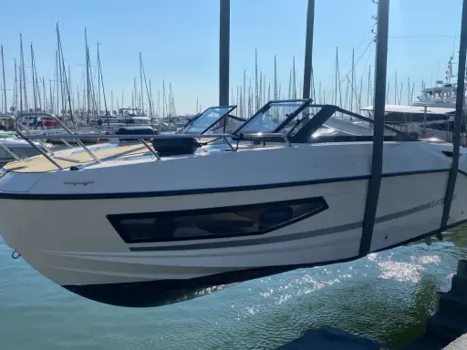 Un bateau blanc est soulevé par une grue, sa coque reflétant le soleil sur la surface mouillée du port.